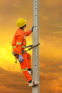 Man holding orange umbrella against sky during sunset