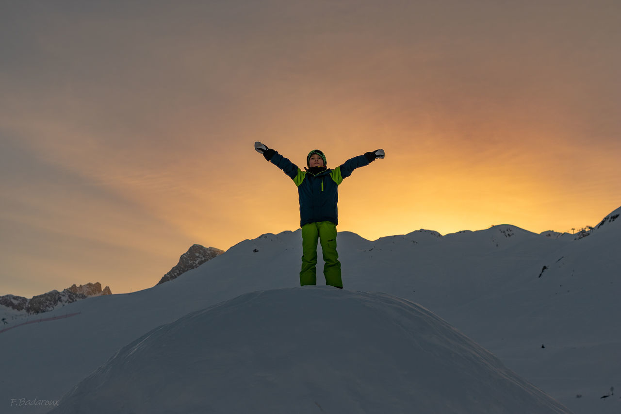 human arm, one person, real people, standing, sky, arms raised, leisure activity, beauty in nature, snow, scenics - nature, winter, cold temperature, limb, sunset, mountain, freedom, lifestyles, vacations, holiday, trip, arms outstretched, warm clothing