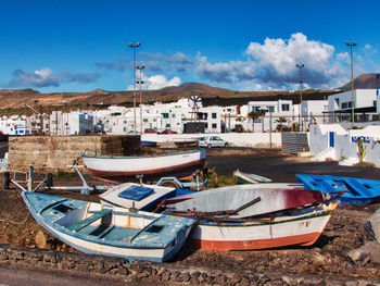 Boats moored on beach by buildings against blue sky