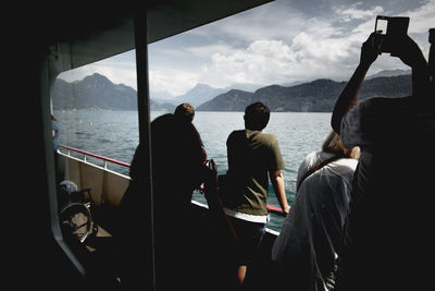 Rear view of people standing in boat on sea against sky