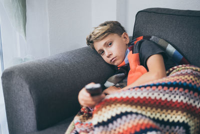 Portrait of ill boy watching tv while lying on sofa at home