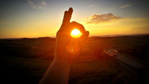 Close-up of hand holding sun during sunset