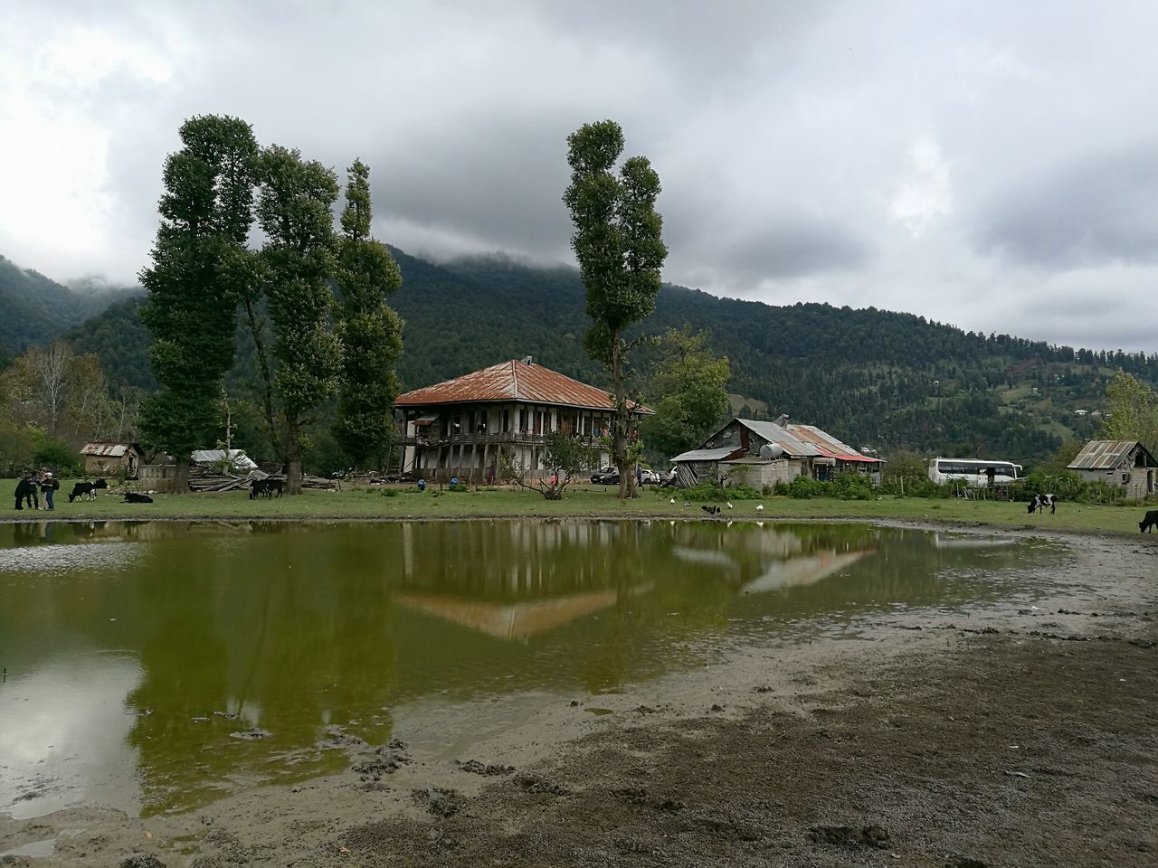 architecture, built structure, water, cloud - sky, building exterior, tree, sky, mountain, cloudy, house, scenics, tranquility, tranquil scene, nature, reflection, beauty in nature, waterfront, remote, outdoors, in front of, non-urban scene, no people, green color, solitude, mountain range