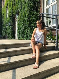 Full length of woman looking away while siting on staircase