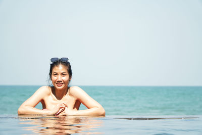 Asian woman relaxing at the luxurious swimming pool by the turquoise sea beach.