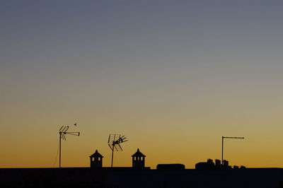 Low angle view of silhouette chimney and antenna against clear sky during sunset