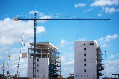 Building under construction with a crane and a blue sky and white clouds.