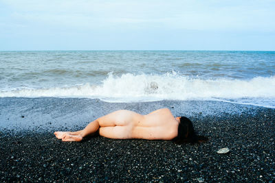 Midsection of young woman on beach against sky