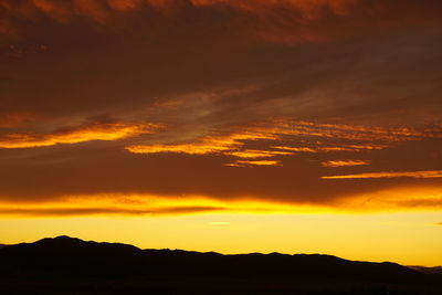 Scenic view of dramatic sky over silhouette landscape during sunset