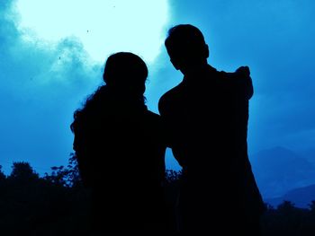 Silhouette man and woman standing against blue sky