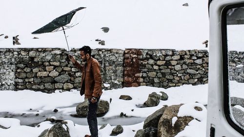 Happy man with damaged umbrella standing on snow covered landscape during winter