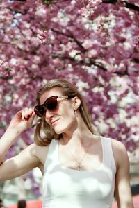 Portrait of young woman wearing sunglasses against pink cherry blossom