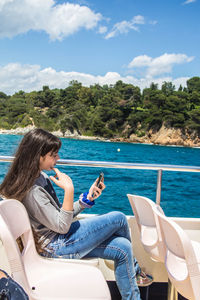 Side view of young woman using mobile phone while traveling in boat