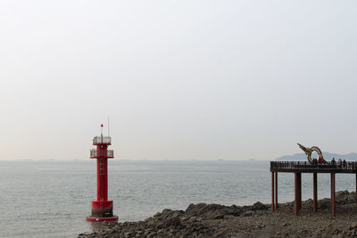 Lighthouse by sea against clear sky