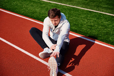 Man in sport clothers does a warm-up exercises at stadium track before jogging outdoors