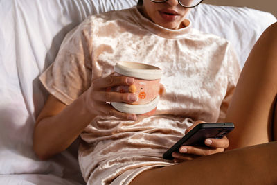 Midsection of woman using phone while lying on bed at home