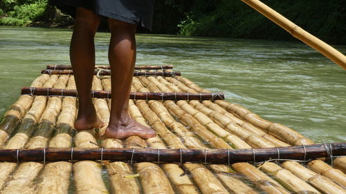 Low section of person standing on bamboo boat in lake