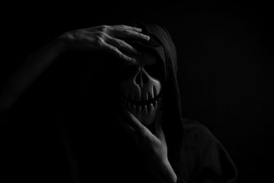 Close-up of person wearing mask standing against black background