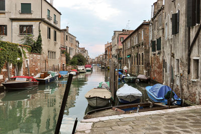 Boats moored in canal amidst buildings in city against sky