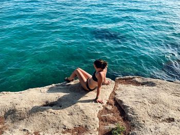 High angle view of shirtless man sitting on rock in sea