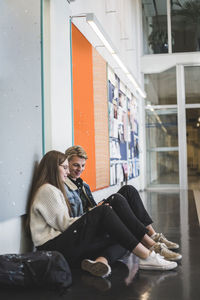 Young man sitting with female friend in corridor of university