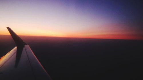 Airplane wing against sky during sunset