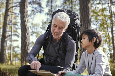 Father and daughter sitting on tree in forest