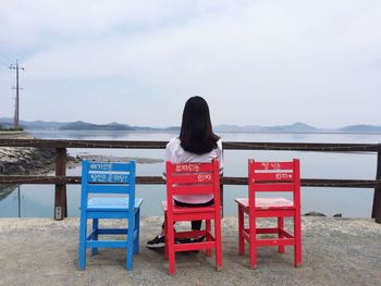 Rear view of woman sitting on chair at beach