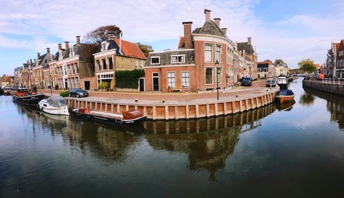 Boats moored in canal by buildings against sky in city