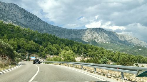 Road amidst trees and mountains against sky