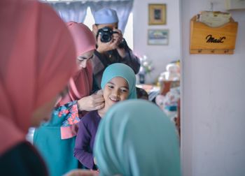 Mother helping daughter in getting dressed by mirror at home