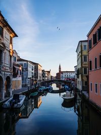 Boats moored on canal in city against sky