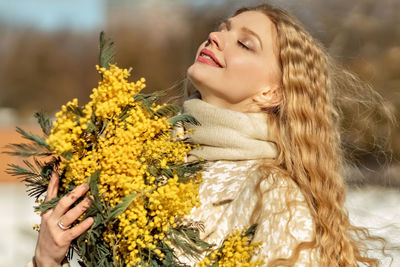 Portrait of a young woman with blond hair holding a bouquet of mimosa in her hands. spring.