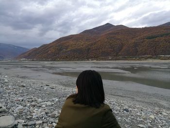 Rear view of woman at riverbank against mountains