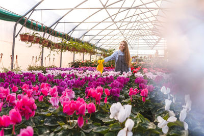 Woman standing by flowering plants in greenhouse