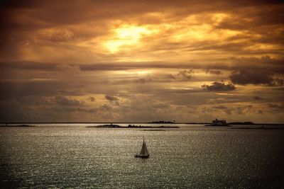 Boat sailing in sea against cloudy orange sky during sunset