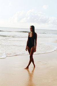 Portrait of young woman standing on beach against sky