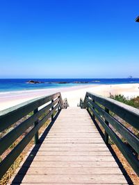 Wooden pier on sea against clear blue sky