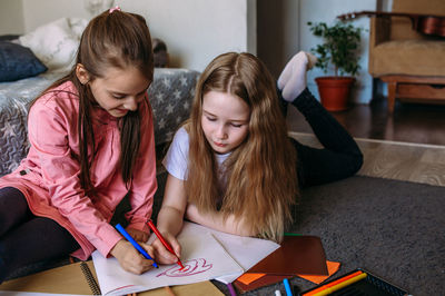 Two girls friends play at home, draw with pencils and felt-tip pens and have fun