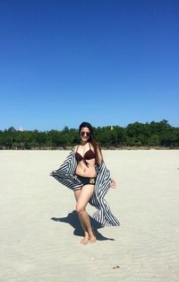 Full length of beautiful young woman on beach against clear sky