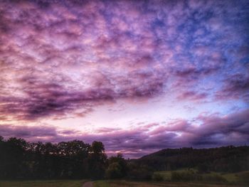 Silhouette trees on field against dramatic sky