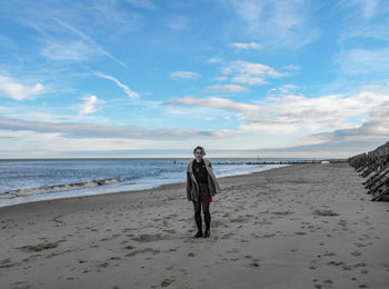 Rear view of woman standing on beach against sky