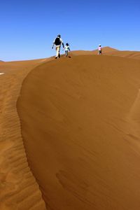 Man on sand dune in desert against clear sky