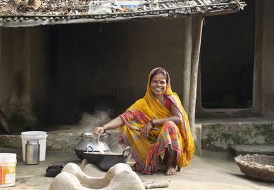 Portrait of smiling indian woman wearing sari making food on traditional chulha or firewood stove