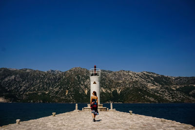 People on rock by sea against clear blue sky