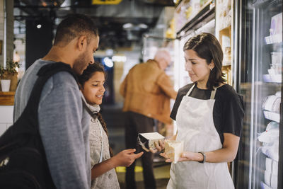 Saleswoman showing cheese to customers at store