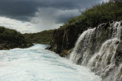 Scenic view of waterfall by sea against sky