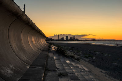 Footpath by sea against sky during sunset