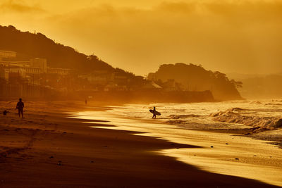 People at beach with silhouette people against orange sky during sunrise