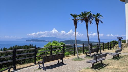 Park bench by sea against blue sky